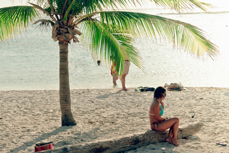Oranjestad, Aruba - January 5, 2018 - A woman sit on a trunk under a palm tree in the beautiful Baby Beach in Aruba.のeditorial素材