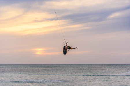 Oranjestad, Aruba - January 16, 2018:A sporty man does acrobatics while practicing kitesurfing at sunset in Aruba.の写真素材