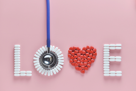 LOVE word made from medicine pills, red heart shape and stethoscope, on pink background. Copy space, Concept of Valentine's Day or pharmacy, Medical.の写真素材