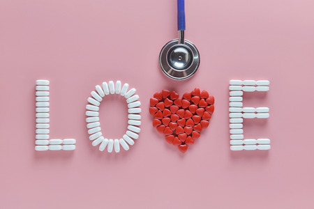LOVE word made from medicine pills, red heart shape and stethoscope, on pink background. Concept of Valentine's Day or pharmacy, Medical.の写真素材