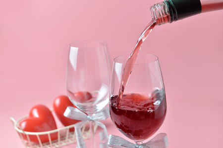 Pouring out of red wine from bottle to glass, with rose at the bottom on pink background. Concept of Valentine's Day, pop art contemporary, celebrate.の写真素材