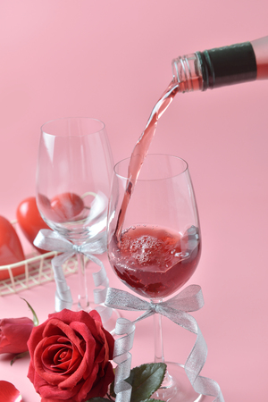 Pouring out of red wine from bottle to glass, with rose at the bottom on pink background. Concept of Valentine's Day, pop art contemporary, celebrate.の写真素材