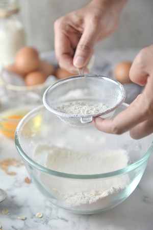 Making pancakes, cake, baking of baker hands sifting flour in bowl. Concept of Cooking ingredients and method on white marble table. Dessert recipes and homemade.の写真素材