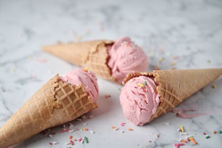Delicious strawberry ice cream cone decorated with sugar rainbow sprinkles on marble background.の写真素材