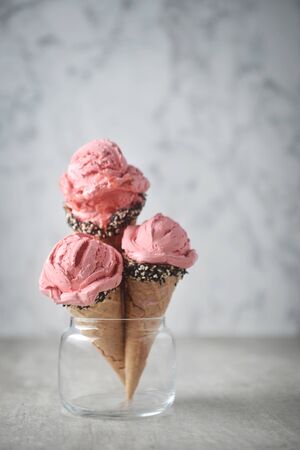 strawberry ice cream and waffle cone decorated with white sesame and black sesame in glass on ground on concrete background.の写真素材
