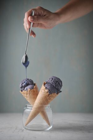 Delicious purple ice cream cone in glass and pouring sauce on plain background.の写真素材