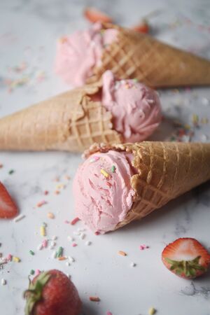Delicious strawberry ice cream cone decorated with sugar rainbow sprinkles and fresh strawberry on marble background.の写真素材