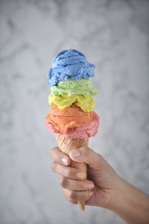 Women hand holding Rainbow ice cream cone on marble background.の写真素材