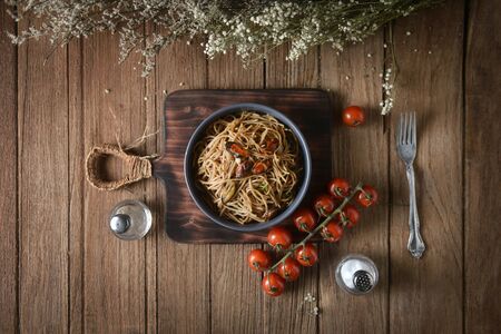 Tasty Italian spaghetti pasta with mussel, tomato and garnish on round dish and wooden plate for serving on wooden table background. top view, horizontal, imageの写真素材
