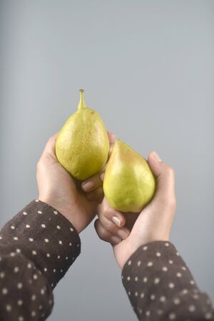 Pear fruit on women hands with brown coat on light grey background. vertical imageの写真素材