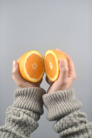 Orange half cut 2 pieces on women hands with sweater on light grey background. vertical image.の写真素材