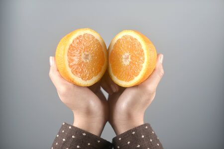 Orange half cut 2 pieces on women hands with brown coat on light grey background. horizontal image.の写真素材