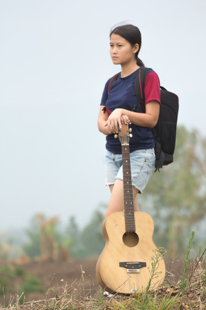 Young woman standing holding a guitar on a high mountain.の写真素材