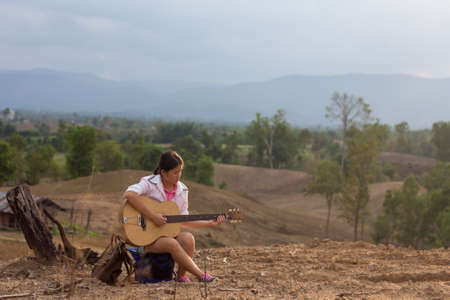 Old girl playing the old guitar on the backdrop is an area for farming, the forest disappears.の写真素材