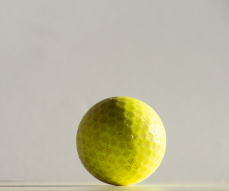 Old yellow golf ball on white backdrop.の写真素材
