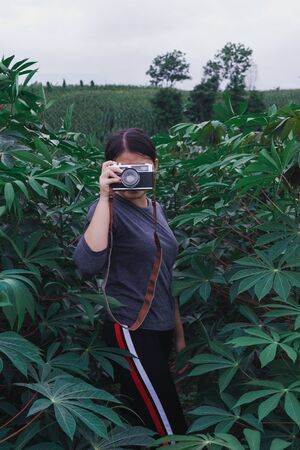 Young women travel on cassava fields, hold old cameras, take pictures.