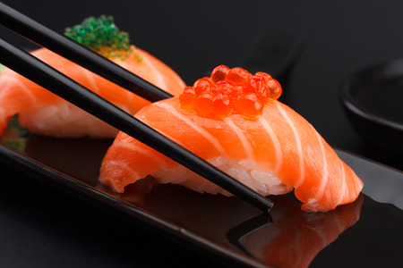Salmon sushi nigiri in chopsticks over black backgroundの写真素材