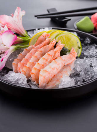 Japanese cuisine, shrimp Sashimi with ice with ginger and wasabi on a black plateの写真素材