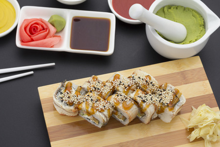 Japanese cuisine. Eel sushi roll on a wooden plate with ginger wasabi over black backgroundの写真素材