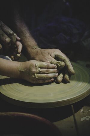 A men's hands guiding a child hands to help him to work with raw clayの写真素材