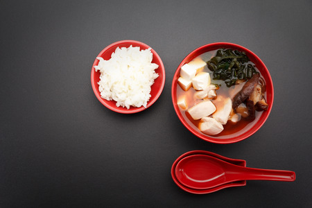 Japanese miso soup and rice on a red bowl and spoon on the table.の写真素材