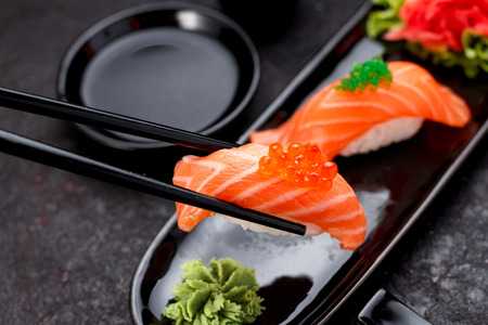 Japanese cuisine. Salmon sushi nigiri on a black plate with chopsticks.の写真素材