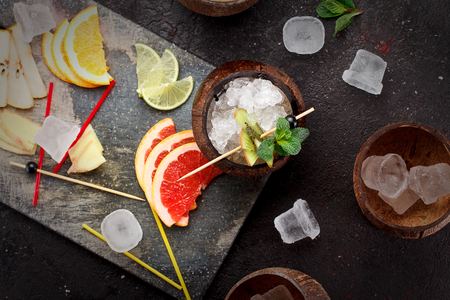 Coconut with ice and fresh fruits (grapefruit, kiwi, orange ) and mint over concrete background.の写真素材