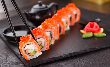 Japanese cuisine. Salmon sushi roll in chopsticks on a stone plate over concrete background.の写真素材