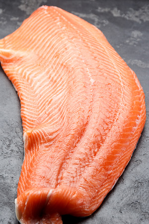 Fresh raw salmon fillet with chef knife over dark stone backgroundの写真素材