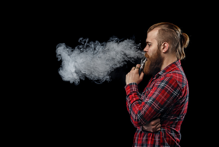 Vaping man holding a mod. A cloud of vapor. Black background. Studio shooting.の写真素材
