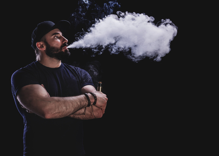 Handsome athletic man is vaping an e-cigarette. Black background. Studio shooting.の写真素材