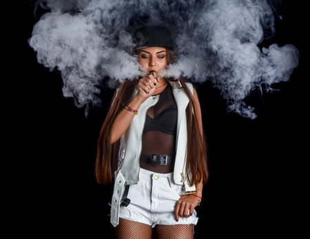 Young and very attractive woman is vaping an e-cigarette. Studio shooting.の写真素材