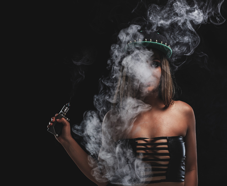 Sexy girl is vaping an e-cigarette. Black background.の写真素材