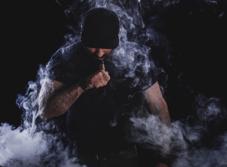 Handsome athletic man is vaping an e-cigarette. Black background. Studio shooting.の写真素材
