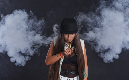 Young and very attractive woman is vaping an e-cigarette. Studio shooting.の写真素材