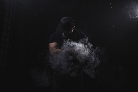 Handsome athletic man is vaping an e-cigarette. Black background. Studio shooting.の写真素材