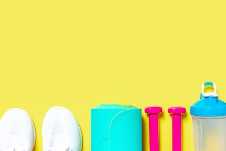 Flat Lay Sport and fitness equipment, pink dumbbells, sneakers, water blender bottle and mint yoga mat on yellow background. Top view with copy space. Healthy lifestyle.の写真素材