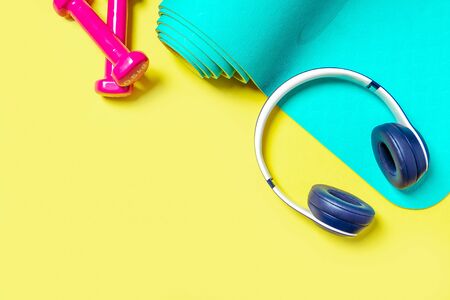Flat Lay Sport and fitness equipment, pink dumbbells, headphones and mint yoga mat on yellow background. View from above with space for textの写真素材