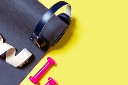 Flat Lay Sport and fitness equipment, pink dumbbells, headphones, black yoga mat and yoga strap on...