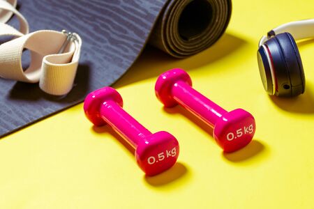 Flat Lay Sport and fitness equipment, pink dumbbells, headphones and mint yoga mat on yellow background. View from above with space for textの写真素材