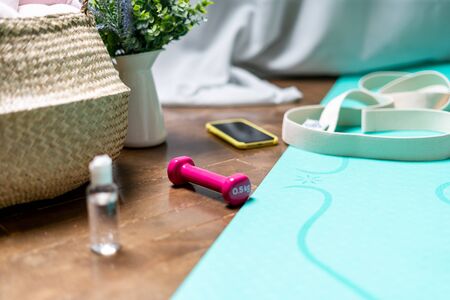 Sport equipment at home, dumbbells, yoga mat, belt and sanitizer on the floor. Fitness isolation period. Weight and health control during quarantine coronavirus. Yoga day conceptの写真素材