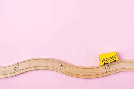 Flat lay back to school composition with yellow school bus model and wooden road on pink background....
