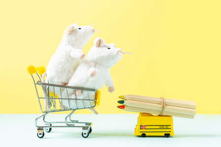Back to school Composition with yellow school bus model with wooden color pencils and two white mouse in the shopping cart on yellow background. Transport for students. With space for textの写真素材