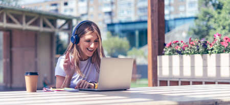 Woman in headphones having a video call with laptop. Happy and smiling girl working outside and...