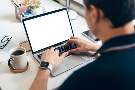 Cropped man typing on mockup laptop computer while sitting at home. Close up human hands and coffee...