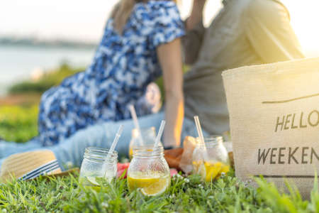 Fresh Homemade Lemonade With lime and lemon On The Grass in sunny park. Blurred green grass and people background. Outdoors Picnic, relaxation concept. Hello weekendの写真素材