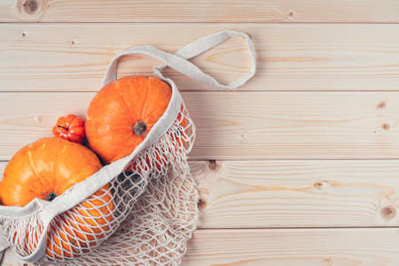 Pumpkins in string shopping bag on wooden background. Copy space for text. Halloween, Thanksgiving day or seasonal autumnal. Design mock up background. Flat lay, top view.の写真素材