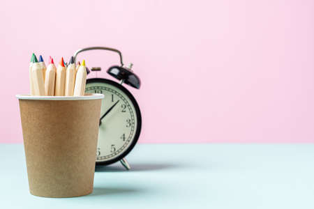 Back to school banner with black alarm clock and pencil in coffee cup stand. School supplies, other elements in pink mint empty background with copy space.の写真素材