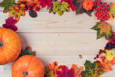 Orange pumpkins, maple leaf, berries and mock up paper blank on wooden background. Hello Fall...