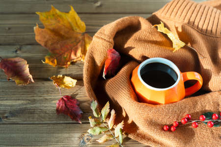 Composition with orange pumpkin styled cup of coffee and autumn themed decoration, fallen leaves, cozy sweater on brown wooden background. copy space.の写真素材